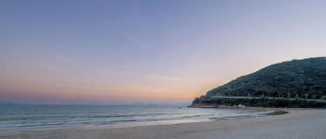 A beach with a gentle slope leading to the water, a clear sky, and a distant hill with vegetation.