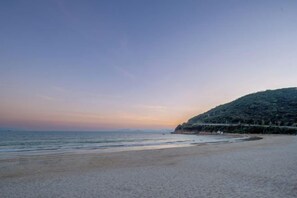 A beach with a gentle slope leading to the water, a clear sky, and a distant hill with vegetation. - Shenzhen Xiyong Resort (Shenzhen)