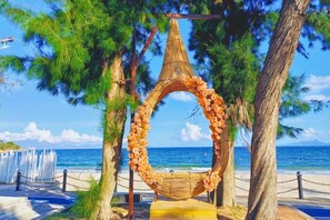 Une plage avec un fauteuil en forme de hamac, entouré d’arbres, d’où l’on a une vue sur l’océan.