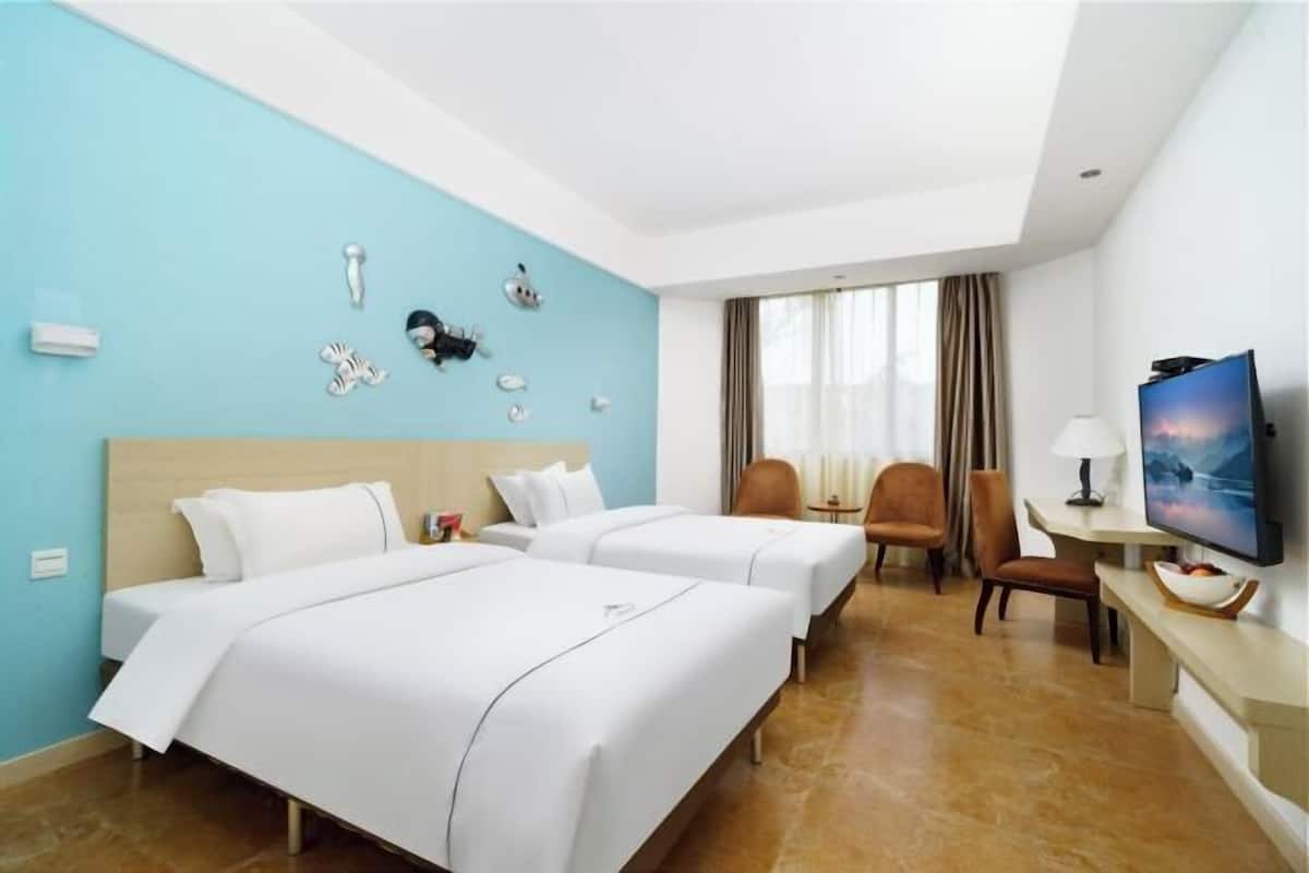Habitación de hotel con dos camas, un escritorio, una silla, un televisor y una ventana con cortinas.