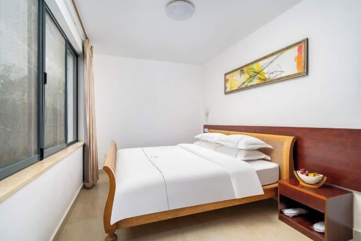 Un dormitorio con cama, ventana, un cuadro y una mesita de noche con un frutero.
