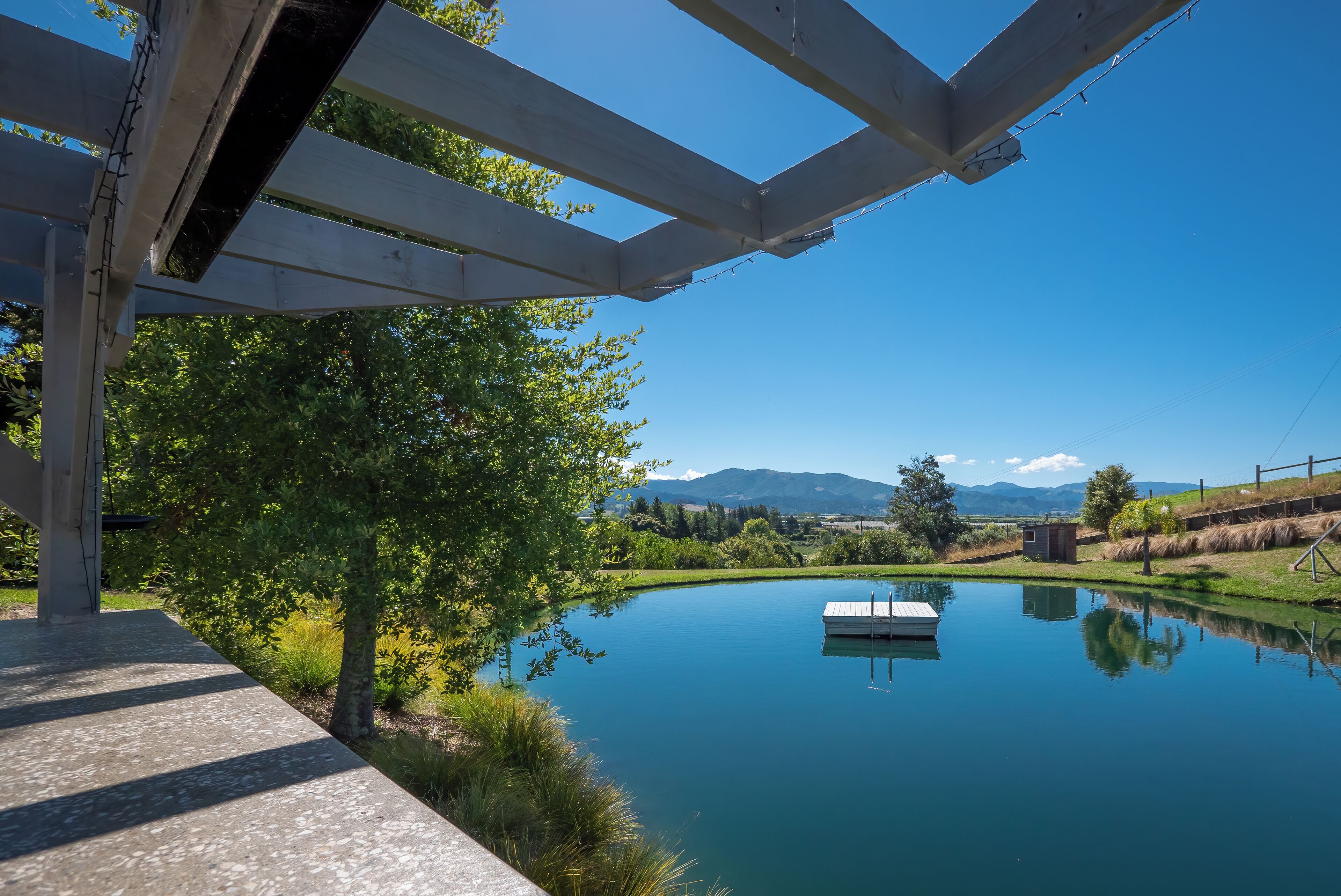 Un espacio al aire libre tranquilo con una pérgola de madera, un lago sereno y un pequeño muelle.
