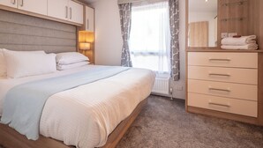 A bedroom with a bed, a wardrobe, a mirror, and a window with curtains.