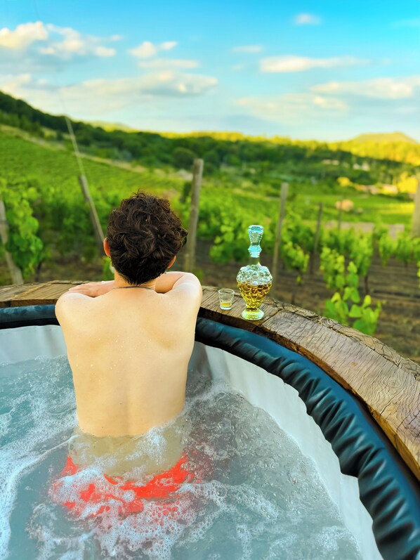 A person relaxing in a hot tub with a vineyard view.