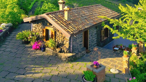 A stone house with a tiled roof, surrounded by a garden with potted plants and a stone pathway. - Mondifeso Chalet (Etna+vineyard+jacuzzi) (Pedara)