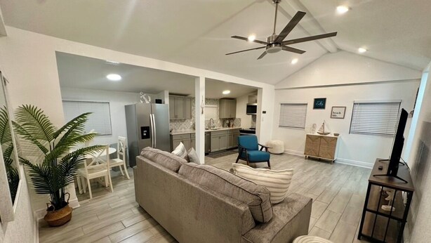Un salón amplio con un sofá beige, una mesa de comedor y una zona de cocina visible a través de un umbral abierto.