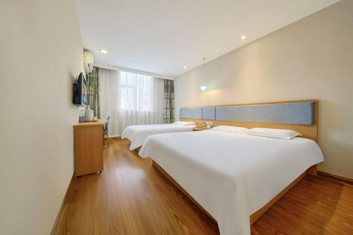 Habitación de hotel con dos camas, piso de madera, un escritorio con silla y una ventana con cortinas.