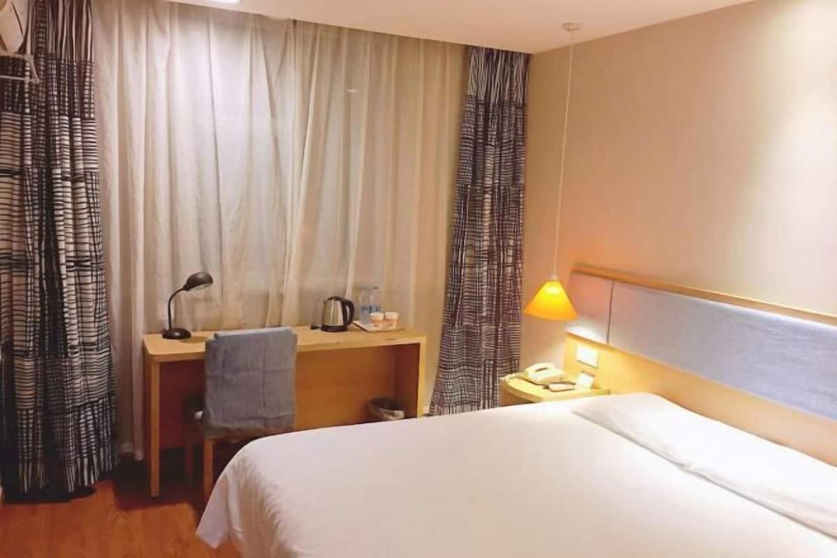 Una habitación de hotel con cama, escritorio con lámpara, teléfono y cortinas.