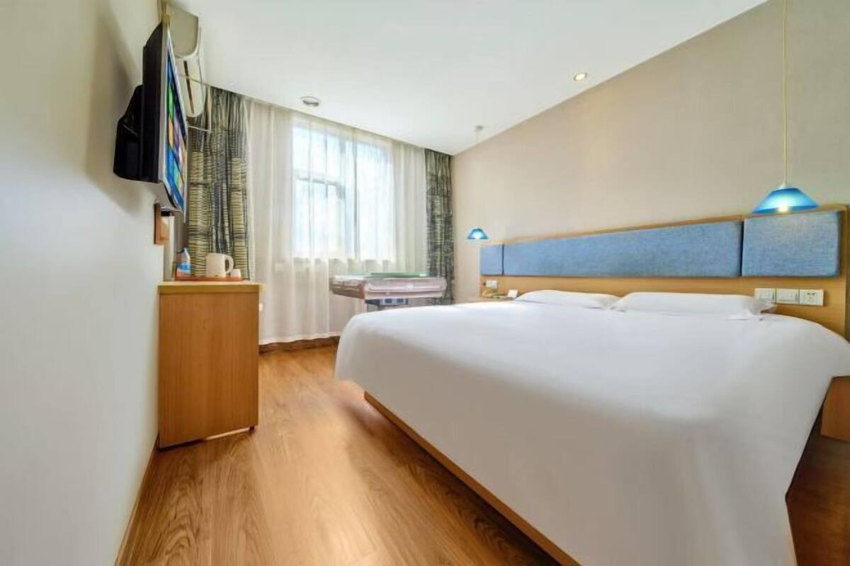 Una habitación de hotel con una cama grande, un escritorio de madera, un televisor y una ventana con cortinas.