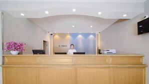 A reception desk with a person behind it, a flat-screen TV mounted on the wall, and a potted plant on the left. - Yuejia Hotel (Shanghai Qingpu District Sports Center Qingpu New City Metro Station Branch) (Shanghai)