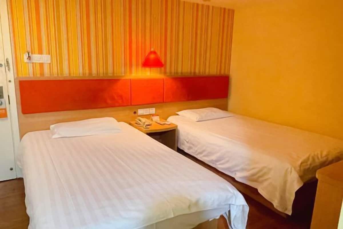 Habitación de hotel con dos camas individuales, una lámpara roja y una cortina a rayas.