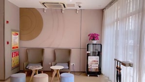 A modern waiting area with two armchairs, a small table, and ottomans. There is a glass display case with items and a window with curtains. - Yuejia Hotel (Shanghai Qingpu District Sports Center Qingpu New City Metro Station Branch) (Shanghai)