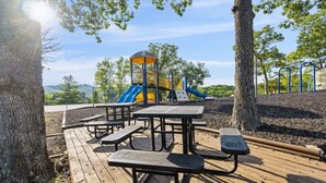 A playground with slides and picnic tables on a wooden deck.