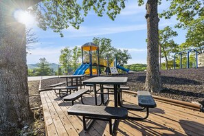 Explore the playground area with a slide and climbing structure, surrounded by trees, and enjoy a picnic at one of the outdoor tables and benches.
