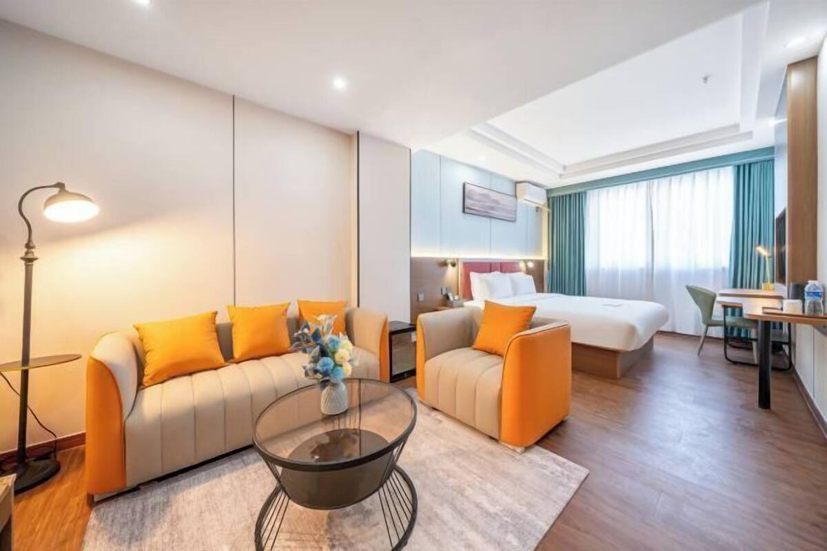 A hotel room with a sofa, a bed, a desk, and a lamp.