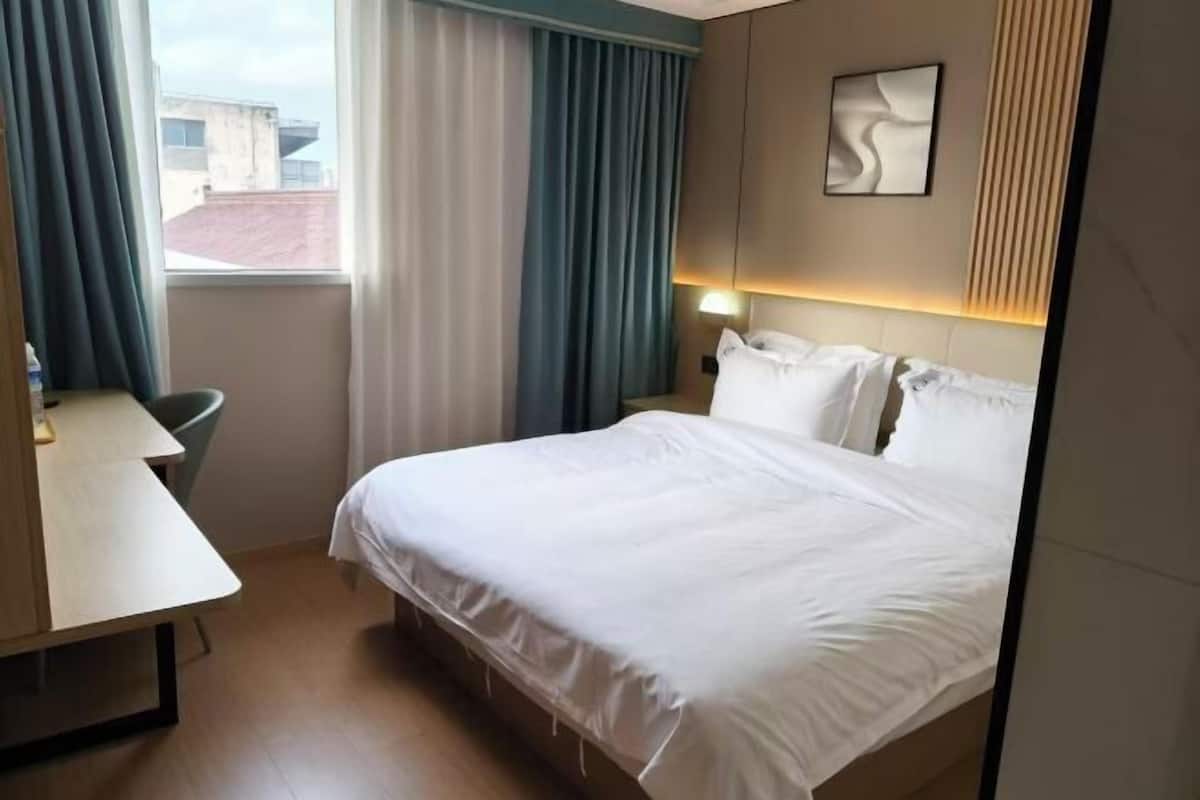 A hotel room with a bed, a desk, a chair, and a window with curtains.