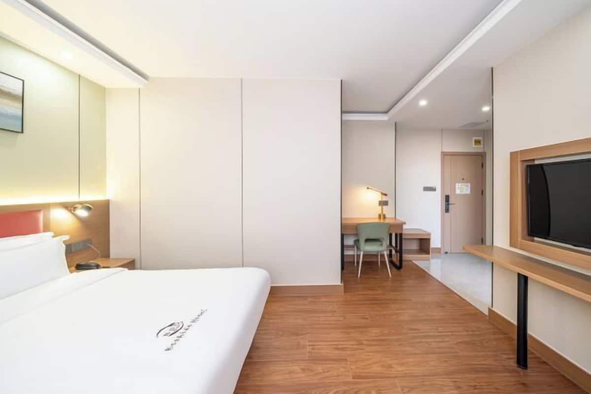 A hotel room with a bed, a desk, a chair, a TV, and a small table.