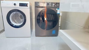 Dos lavadoras de carga frontal en un baño moderno y limpio, con encimera blanca y espejo.
