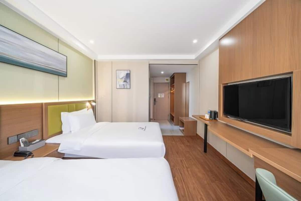 A hotel room with two beds, a TV, a desk, and a painting on the wall.