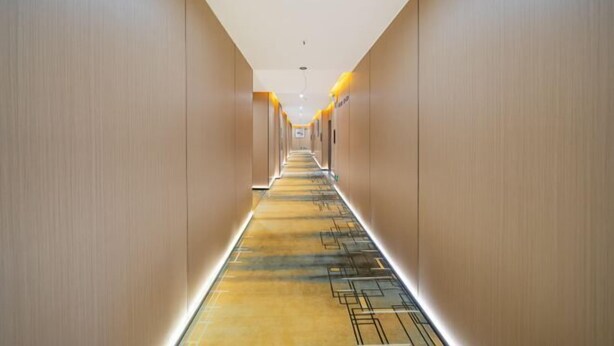 Un pasillo largo y moderno en un hotel, con iluminación empotrada y una alfombra estampada.