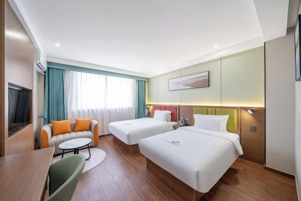 A hotel room with two beds, a sofa, a small table, and a TV.