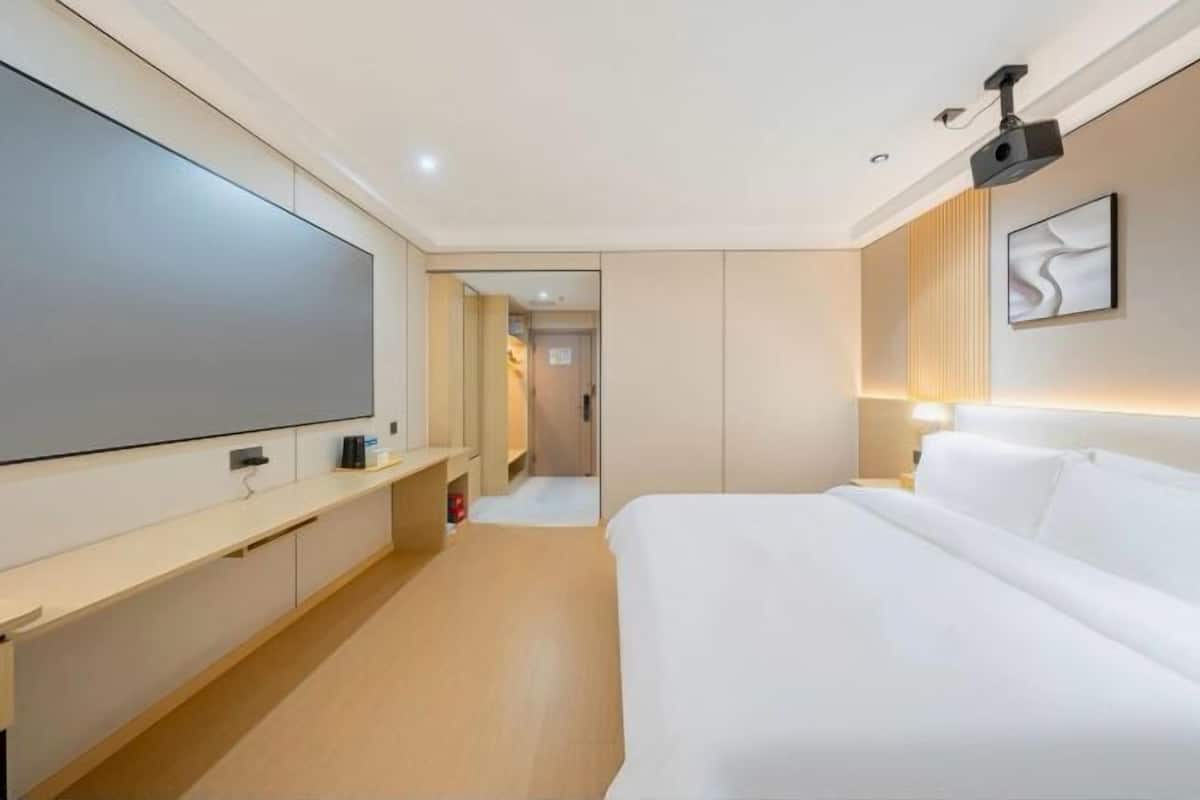 A modern hotel room with a large flat-screen TV, a bed, a bedside table, and a wall-mounted projector.