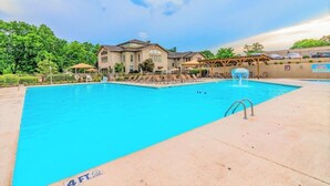 A swimming pool with a 4 FT depth marker, surrounded by a covered patio area with umbrellas and a pergola. - Pointe Royale Resort | Golf, Indoor Pool & More (Branson)