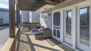 Eine überdachte Terrasse mit Holzgeländer, einem Sitzbereich mit Kissen und einer Schiebeglastür.