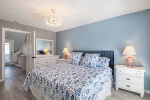 Un dormitorio con una cama, dos mesitas de noche con lámparas, un aparador, un espejo y una escalera que lleva a otra habitación.