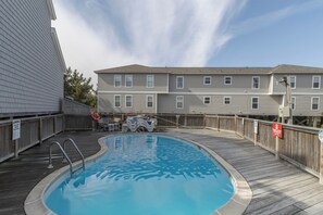 Una piscina con plataforma de madera, rodeada por una cerca de madera, junto a un edificio con varias ventanas.