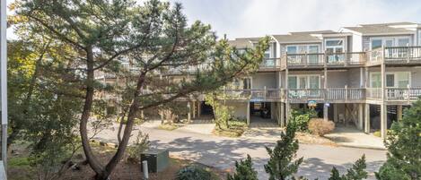 A multi-story building with balconies, a covered walkway, and a parking area.
