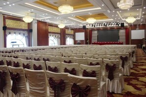A banquet hall with rows of chairs, a stage, and a large screen. - Huidu Hotel (Longmen)