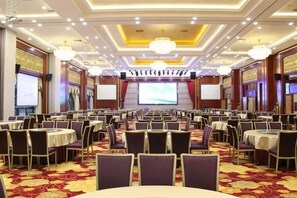 A conference room with round tables and chairs, a large screen, and a stage. - Huidu Hotel (Longmen)
