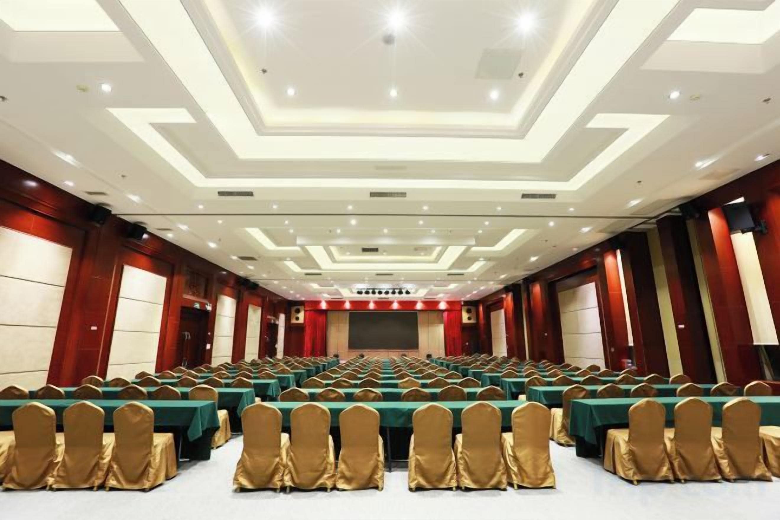 A conference room with rows of tables and chairs, a stage, and a large screen.