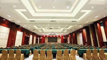 A conference room with rows of tables and chairs, a stage, and a large screen.
