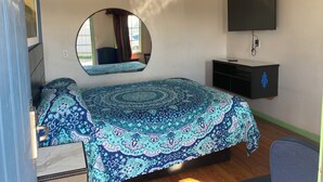 A bedroom with a bed, a TV mounted on the wall, and a mirror above the bed.