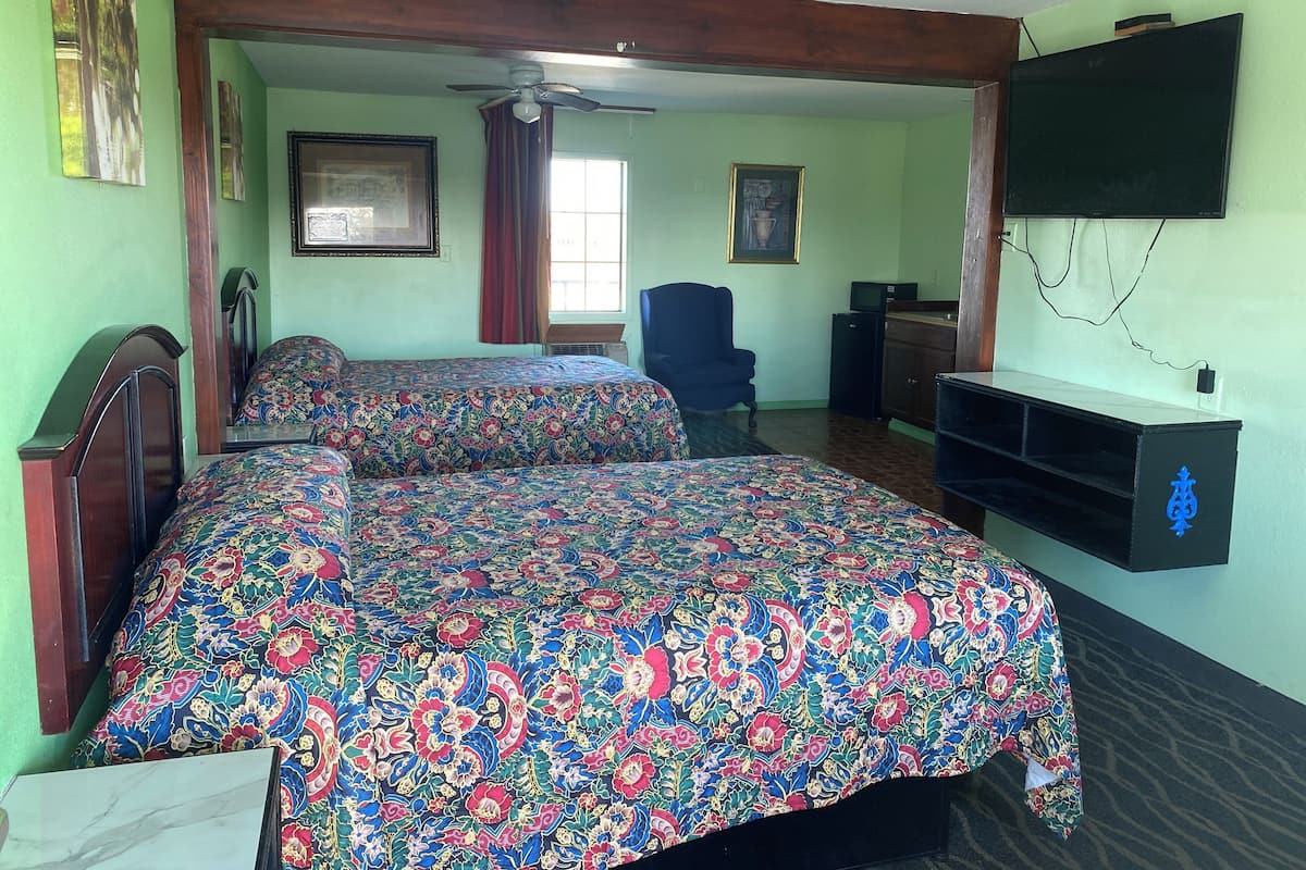 A room with two beds, a ceiling fan, a TV, and a desk with a computer.