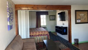 A room with a sofa, a bed with patterned bedding, a television mounted on the wall, and a framed picture.