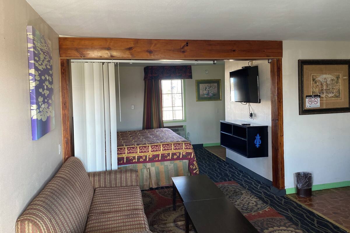 A room with a sofa, a bed with patterned bedding, a television mounted on the wall, and a framed picture.