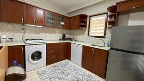 Eine Küche mit Holzausstattung, einer Waschmaschine, einem Geschirrspüler, einem Kühlschrank und einem Fenster mit Jalousien.