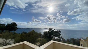 Ein Balkon mit Blick auf das Meer und das ferne Land, ein klarer Himmel darüber.