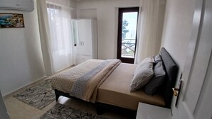 Ein Schlafzimmer mit Bett, Kleiderschrank, einem Fenster mit Vorhängen und Balkonblick.