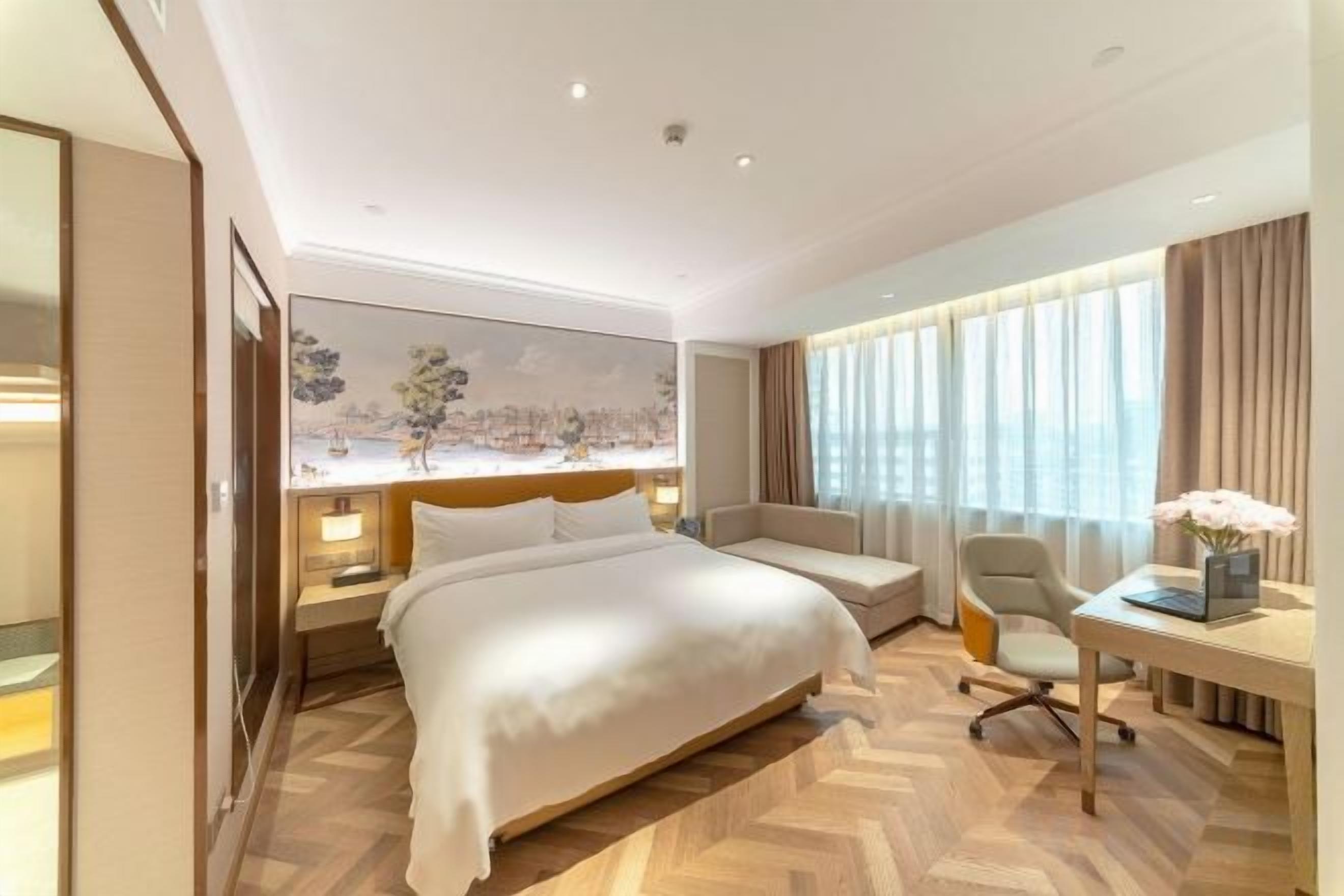 A hotel room with a large bed, a desk, a chair, and a painting on the wall.