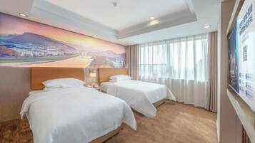 Habitación de hotel con dos camas, un mural grande en la pared y vista a un paisaje urbano a través de la ventana.