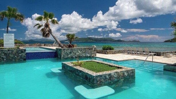 A pool area with clear blue water, palm trees, and a view of the ocean.