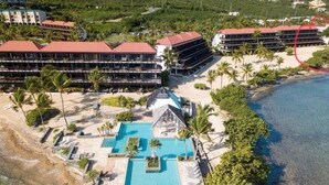 An aerial view of a resort with multiple buildings, a central swimming pool, and a beach area.