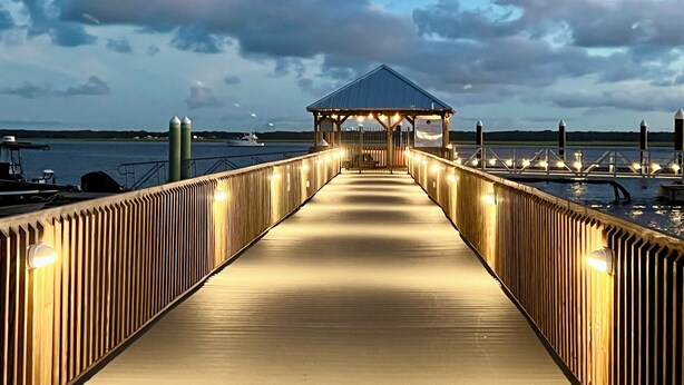 Un muelle de madera que lleva a un quiosco cubierto con luces, con vista a una masa de agua.