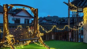 Um baloiço de madeira com luzes, cercado por uma vedação e relva, com edifícios ao fundo.