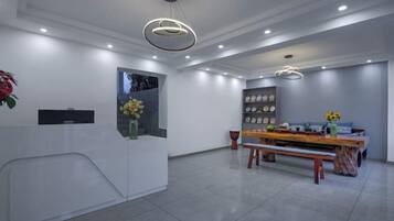 A modern reception area with a reception desk, a bench, a dining table, and a wall-mounted shelf with decorative items.
