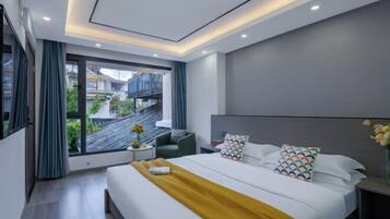 A modern hotel room with a large bed, a small side table, a chair, and a view of the outside balcony.